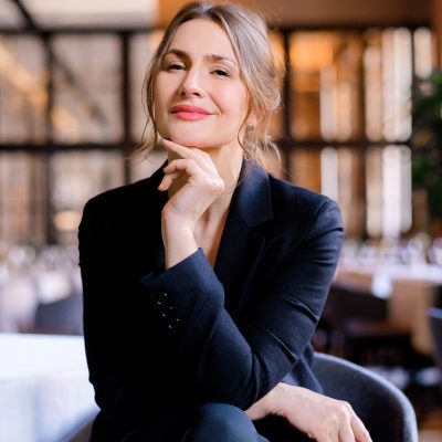 Portrait of smiling successful businesswoman looking into camera sitting in the restaurant. Business lady with stylish hairstyle wears elegant suit. Business meeting. Attractive appearance